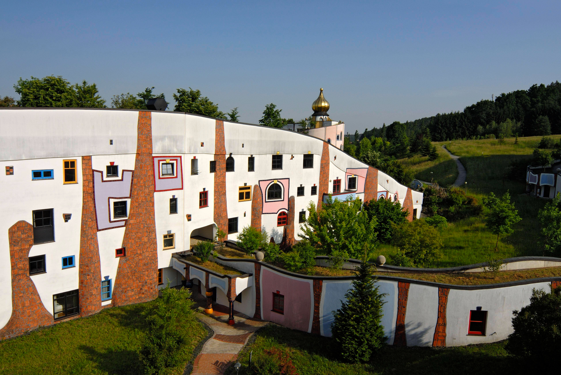 Eingebettet in die hügelige Natur: Die Hundertwasser-Therme Rogner Bad Blumau mit ihren bunten Hotelfenstern